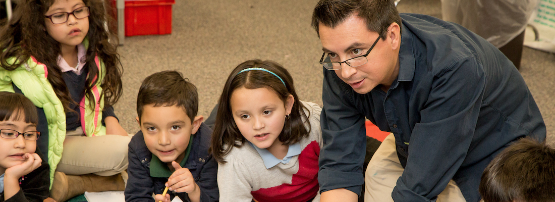 Teacher sitting on the floor with class of students